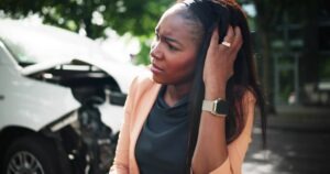 A woman in front of a smashed car, wondering how to get a crash report in Pearland, TX.